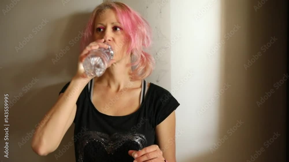 Fit woman portrait in black sportwear, drinking fresh water from a bottle in fitness center, tired after workout. Healthy lifestyle concept. Slow motion. Fit woman portrait in black sportwear, drinking fresh water from a bottle in fitness center, tired after workout. Healthy lifestyle concept. Slow motion.
