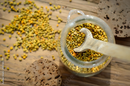 Grains of bee pollen in jar and wooden spoon on wooden table. Apitherapy. Bee products.