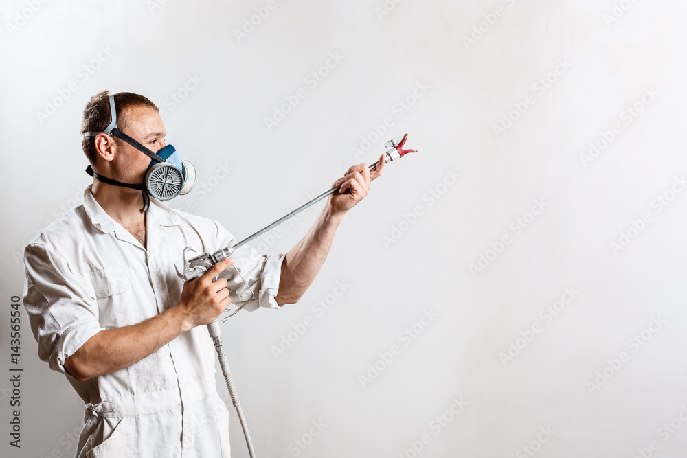 Worker painting wall with spray gun in white color.