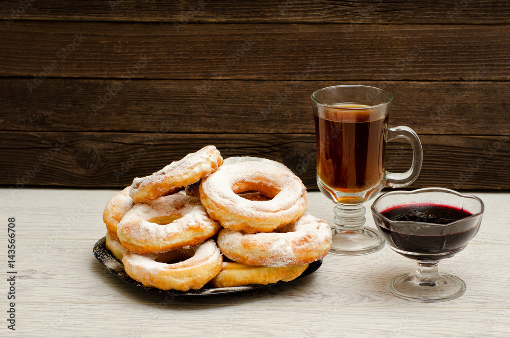 Donuts with icing sugar, a mug of tea and currant jam on a wooden background Donuts with icing sugar, a mug of tea and currant jam on a wooden background