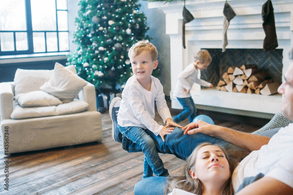 Father and mother lying on the sofa and playing with two little sons Father and mother lying on the sofa and playing with two little sons