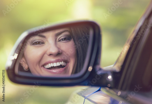 Happy woman driver looking in car side view mirror laughing