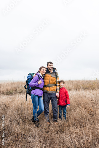 Happy family with backpacks standing in grass
