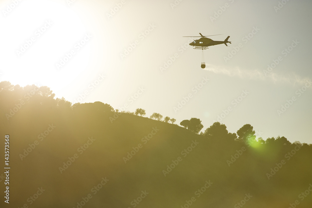 Naklejka premium GRANADA, AUGUST 28: Fire fighting Helicopter, with bambi basket, during a fire fighting in the bush. August 28, 2014, Granada, Spain.