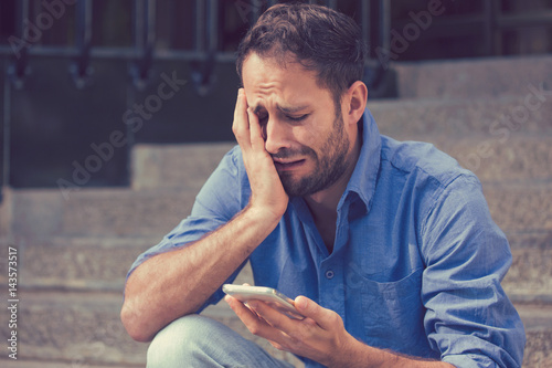 Upset man looking at his mobile phone outdoors photo