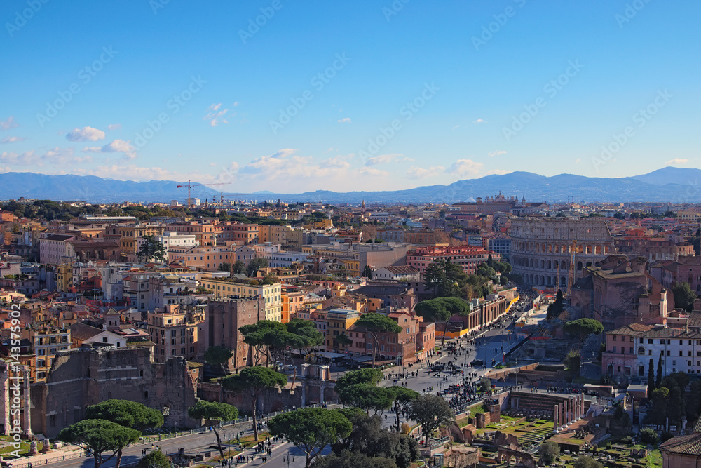 View to rooftops of Rome skyline from the Monument of Vittorio Emanuele II at Piazza Venezia. Rome Forum with ruins of historical buildings. Colosseum in the background. Winter morning view