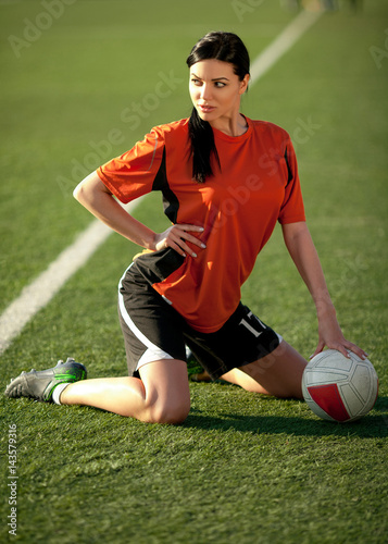 Girl in soccer uniform sitting on football field with ball. © Stanislav