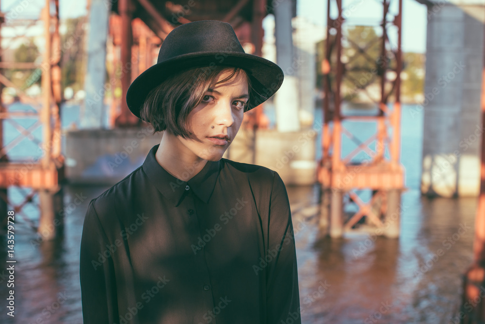 Beauty looking girl with stylish black hat and dress. Urban city street under bridge constructions. Beauty looking girl with stylish black hat and dress. Urban city street under bridge constructions.