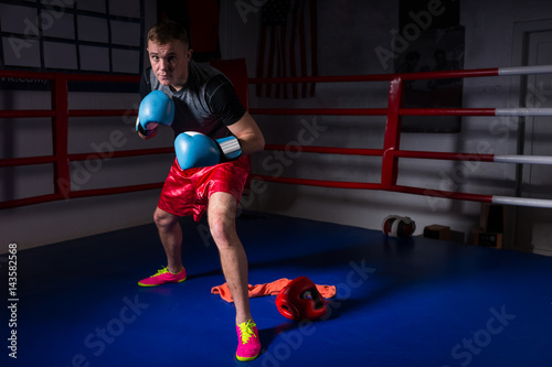 Young sporty male boxer in boxing gloves rises and prepares for battle in regular ring