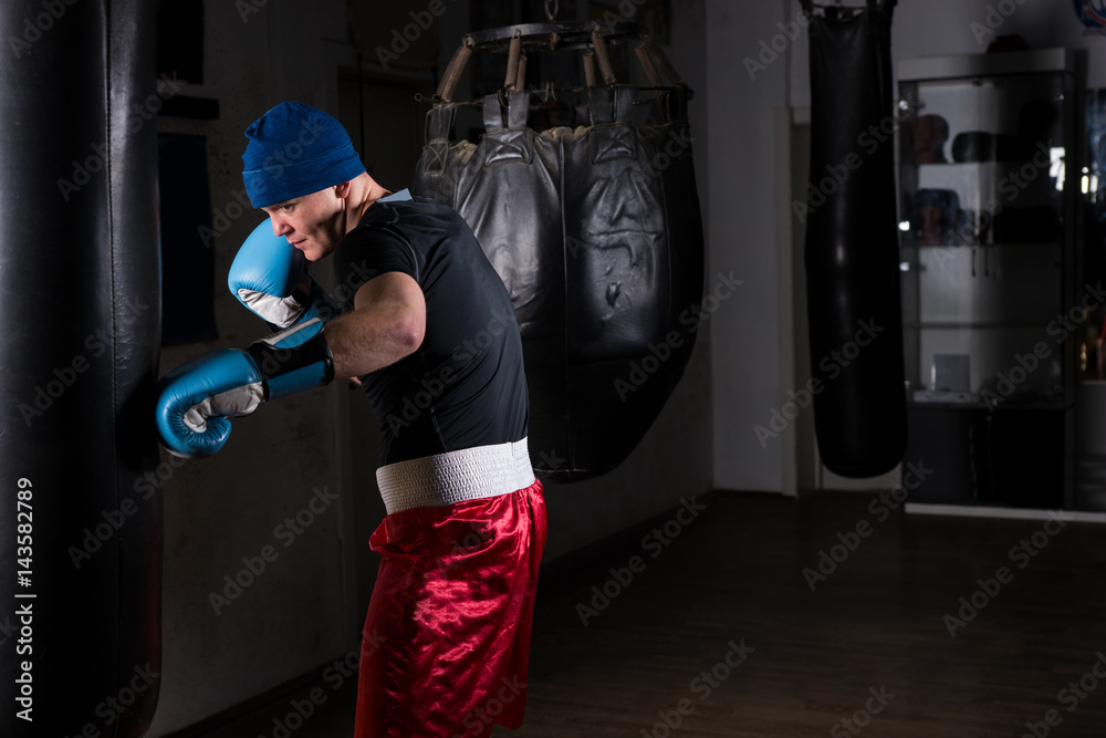 Young male in a hat and boxing gloves training with boxing punching bag