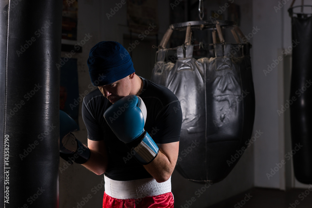Young male boxer in a hat and boxing gloves training with boxing punching bag