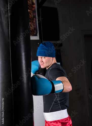 Sporty male boxer in boxing gloves training with boxing punching bag