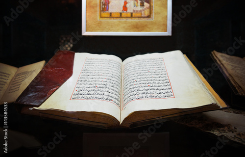 Святая Исламская старая книга Коран открыт в кожаной обложке на фоне других книг и картины 