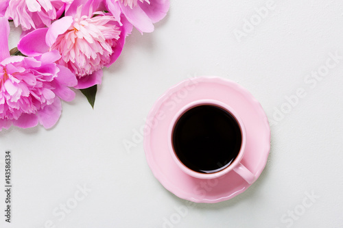 Cup of coffee and flowers (peonies) on light grey table.