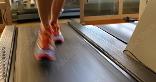 Fitness model woman running on treadmill with muscular legs indoor. Colorful gym shoes of girl on gym tapis roulant. Fast training indoor. Healthy active lifestyle . 4K front close up view. photo