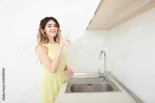 Beautiful young woman holds a glass with water on kitchen