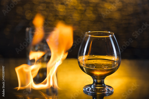 Glass o whisky with ice and wineglass of coghac and fire flames on yellow bokeh background © Алексей Торбеев