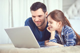 Father and his daughter are looking at the screen of their laptop