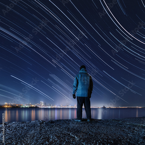 Hiker, standing on the river bank and enjoying a night view of the sky
