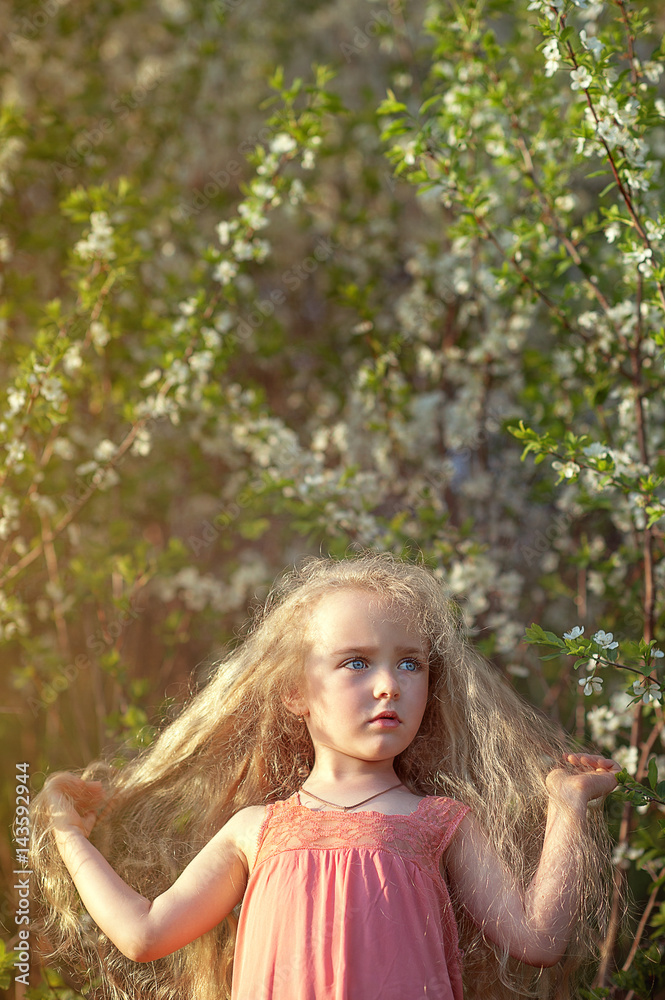 A beautiful little girl with long hair in a flowered garden A beautiful little girl with long hair in a flowered garden