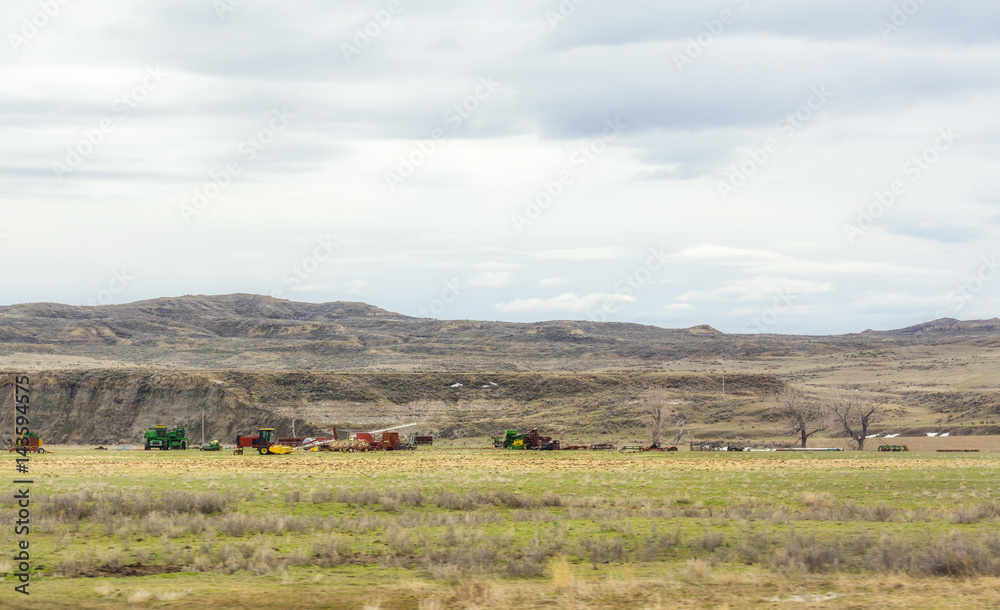Various modern farming equipment parked in a pasture in a valley with mountains and hills in the background in Montana landscape