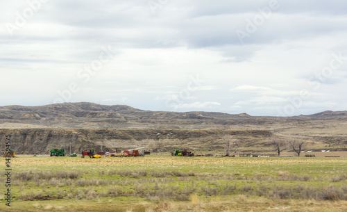 Various modern farming equipment parked in a pasture in a valley with mountains and hills in the background in Montana landscape