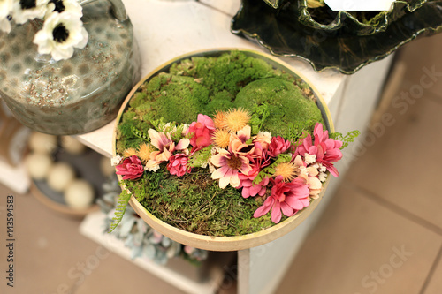 Stroik, dekoracja z kwiatów i mchu w drewnianym talerzu.