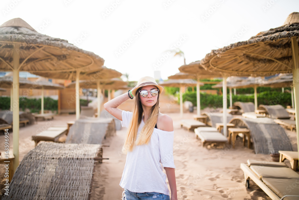 Fototapeta premium Woman walking on a tropical beach holiday. Luxury wooden lounge and sunny outdoors background