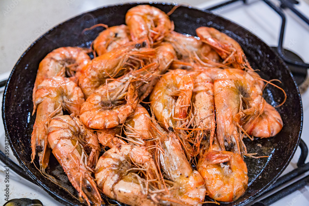 Giant tiger shrimps with heads fried in oil in a frying pan on a gas stove