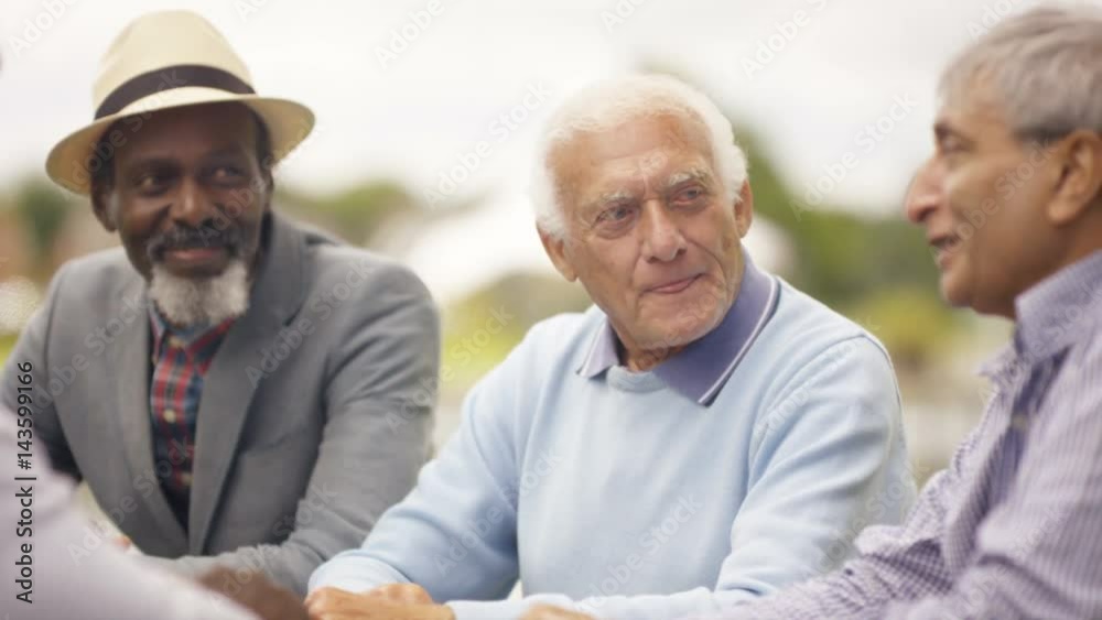 Happy senior male friends chatting & laughing together outdoors in the park Happy senior male friends chatting & laughing together outdoors in the park