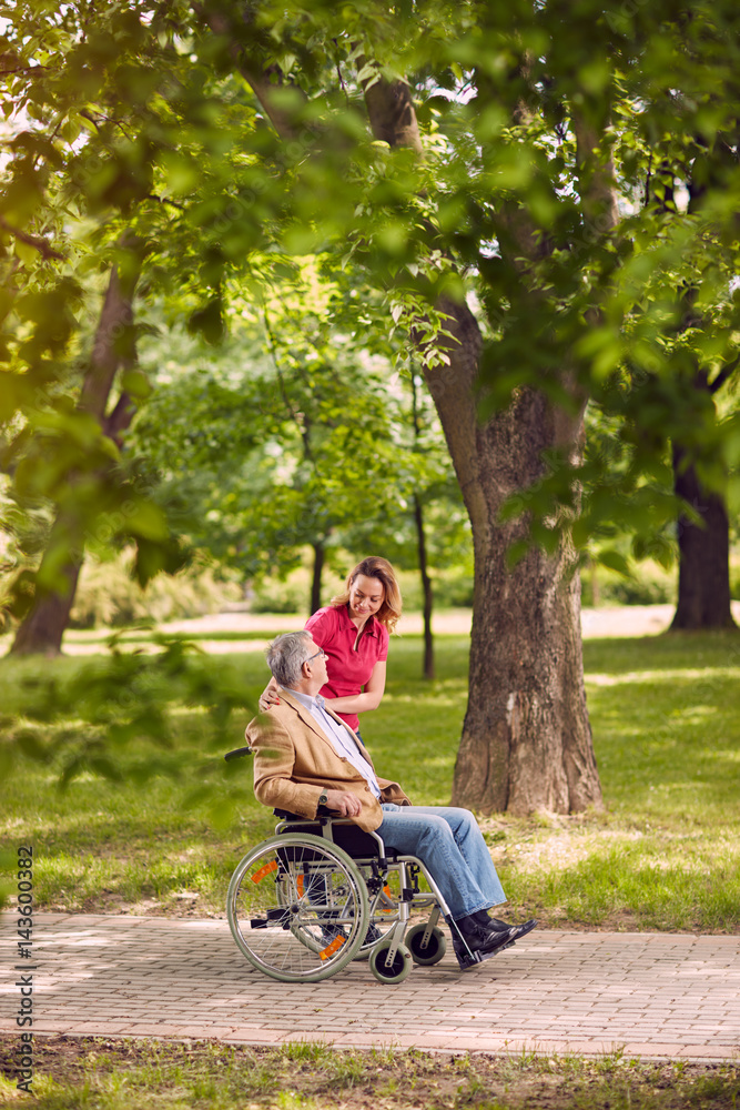 elderly man in wheelchair talking with daughter in the park- happy family time. elderly man in wheelchair talking with daughter in the park- happy family time.