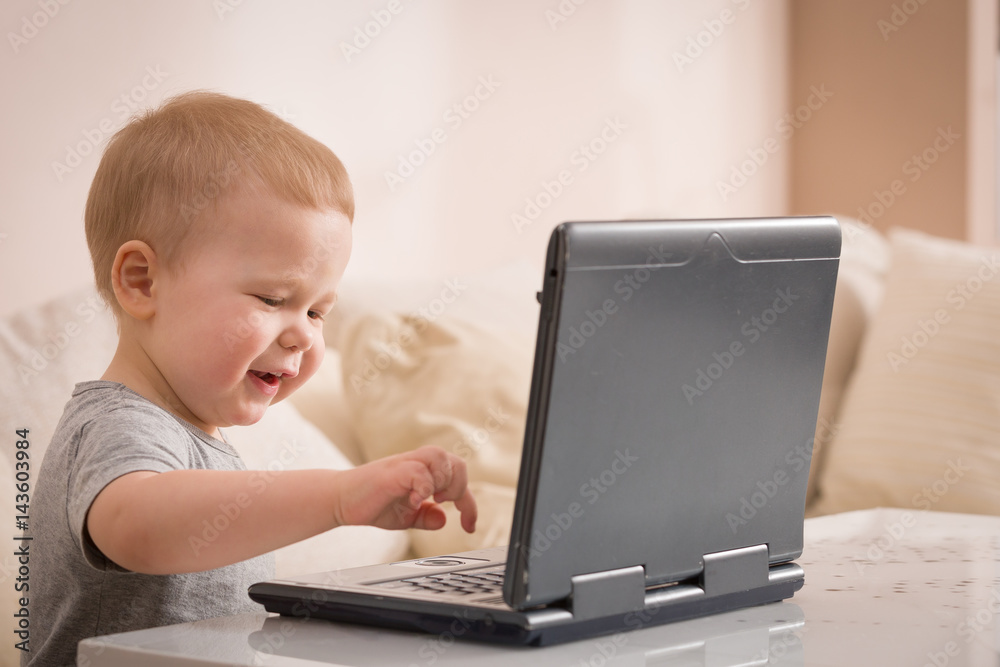 Cute little toddler boy sitting on the sofa with his laptop and looking at the window. Learning with computer. Early development. Child and computer. Cute little toddler boy sitting on the sofa with his laptop and looking at the window. Learning with computer. Early development. Child and computer.