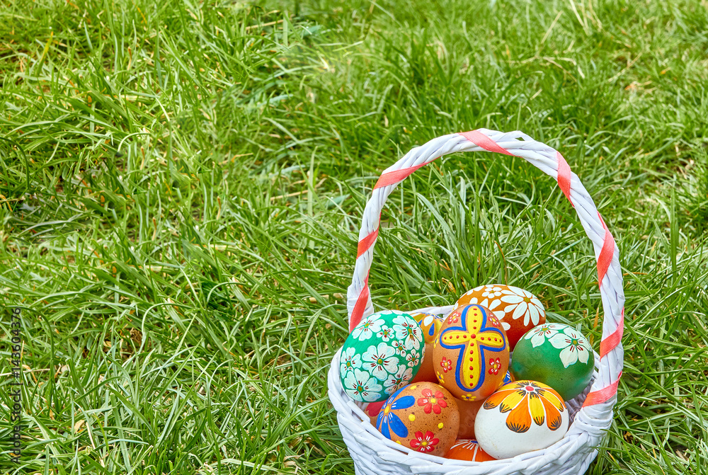 Wicker basket with hand-painted easter eggs on green grass