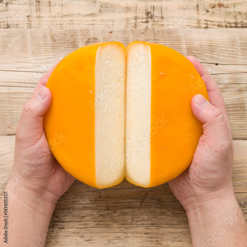 Top view on cut cheese head in yellow vacuum pakage in man's hands on wooden board. Serving French homemade cheese. Food concept photo