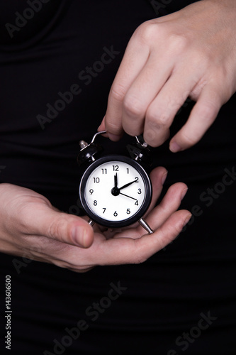 Female hands holding black and white little clock on dark background