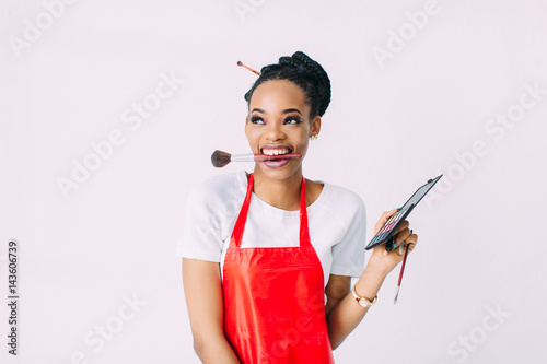 Beautiful young African American beautician woman holding set of make up brushes and eye-shadows photo