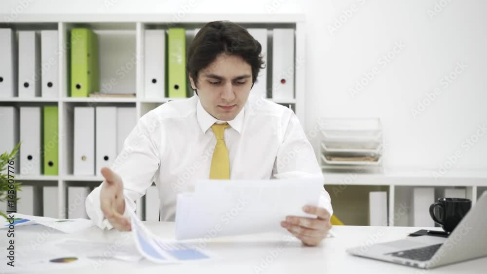 Stressed businessman is sitting at his desk in a white office, looking through papers and throwing them away unsatisfied. Locked down real time medium shot Stressed businessman is sitting at his desk in a white office, looking through papers and throwing them away unsatisfied. Locked down real time medium shot