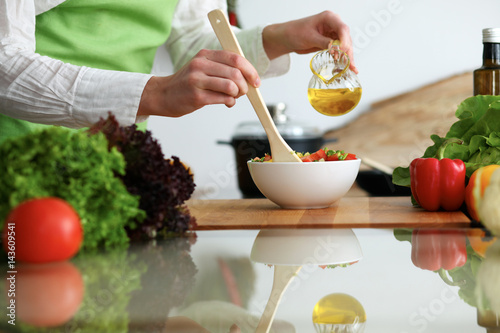 Closeup of human hands cooking vegetables salad in kitchen on the glass table with reflection. Healthy meal and vegetarian concept