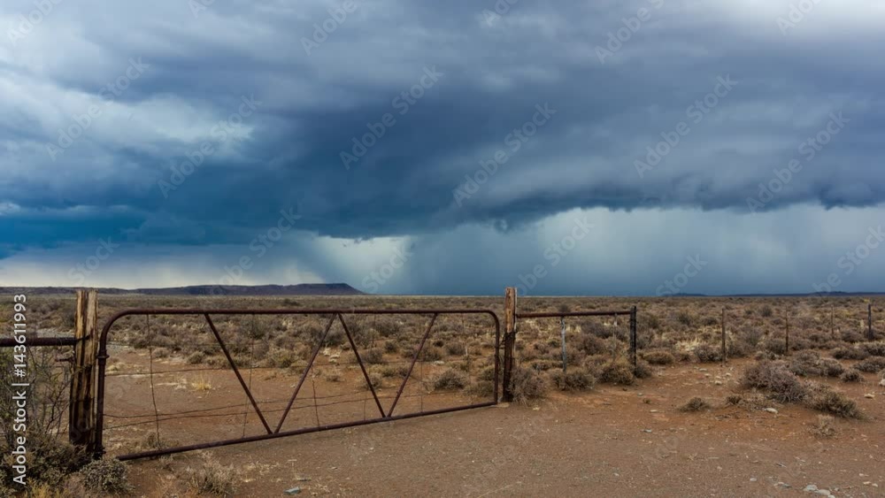 A static timelapse shot of a typical Karoo farm landscape with an old rusted gate and fence while an intense storm is approaching with dark and stormy skies or supercell clouds, South Africa