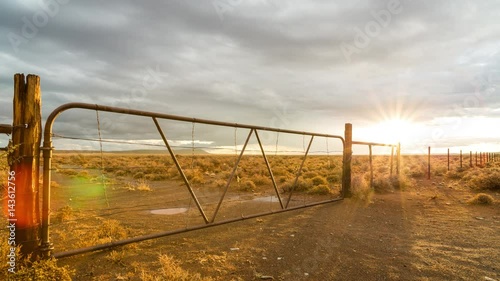 A beautiful static timelapse after a storm with a drenched Karoo landscape of an old rusted gate and fence with puddles of water while the sun dips through the clouds with an intense golden glow