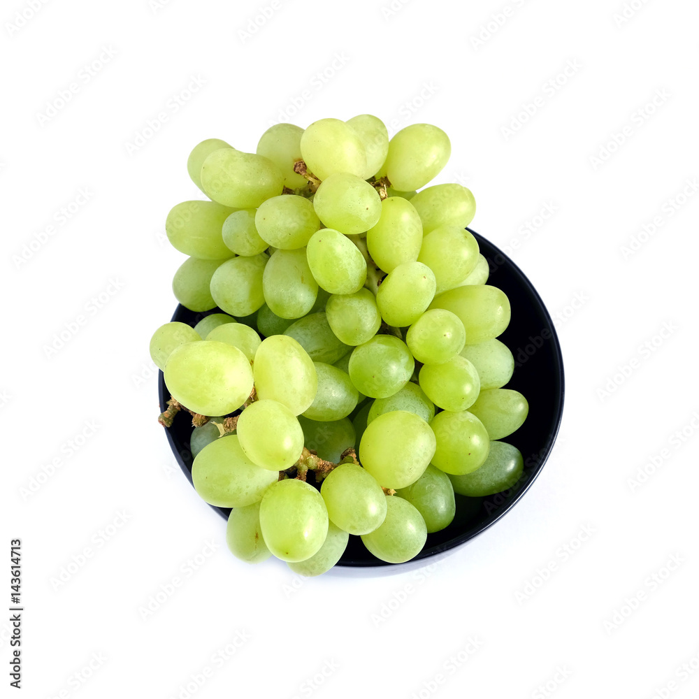 Lot of ripe green grape berries on bunch in black round bowl on white background top view close up