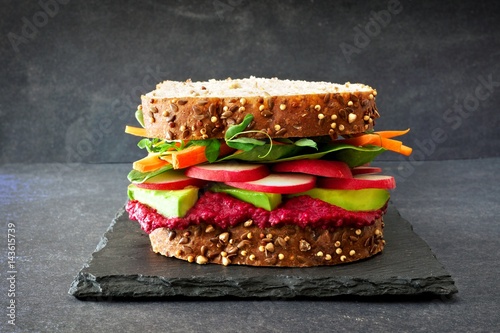 Superfood sandwich with beet hummus, avocado, vegetables and greens, on whole grain bread against a slate background