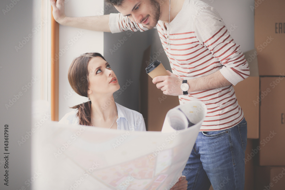 Young couple sitting on the floor and looking at the blueprint of new home - obrazy, fototapety, plakaty 