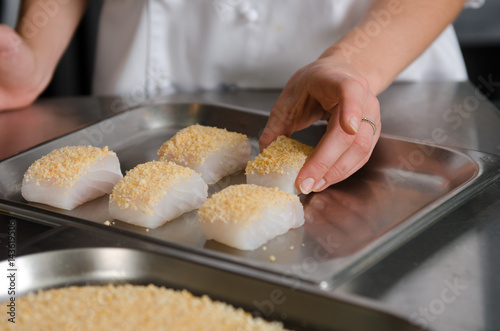 Fresh fish fillet cube covered in breadcrumbs, being placed onto a metal baking tray.