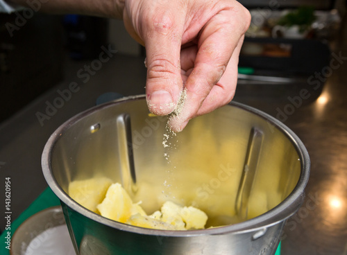 Close up shot of a hand dropping black pepper onto fluffy peeled potatoes into a blender.