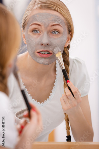 Happy young woman applying mud mask on face