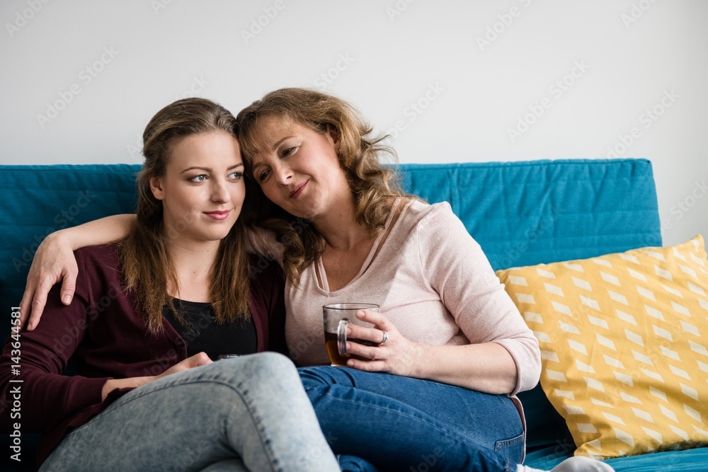 Mother and teenage daughter hugging on sofa at home