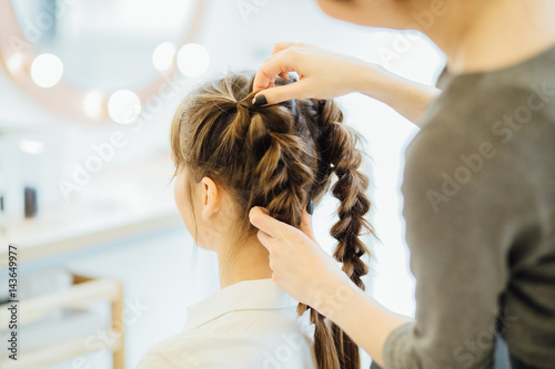 Super styling. Close up of a hairdresser braiding her clients hair in trendy weave plait while sitting in hairdressing salon. European model. Beauty lifestyle concept.
