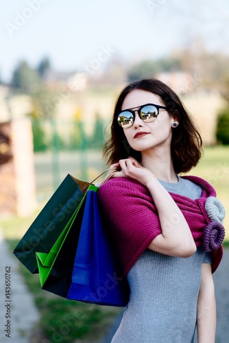 Fashion girl in pink woolen shawl holding paper shopping bags.