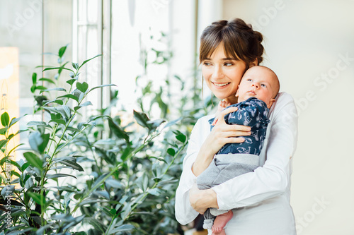 Mother holding newborn baby boy near big window. Motherhood, care and protection concept. photo